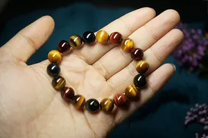 Dettaglio di un bracciale in pietre occhio di tigre rosse, blu e gialle su una mano