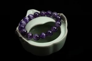 Close-up of a natural dream amethyst bead bracelet displayed on a green porcelain bowl