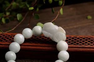 Macro detail of hand-carved jade Pixiu charm and round beads on dark wooden tray
