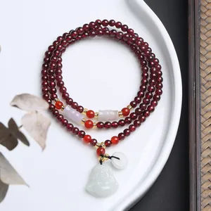 Detailansicht eines mehrlagigen Granat-Armbands mit Jade-Buddha-Anhänger und Goldakzenten