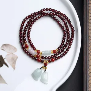 Detail eines Granatperlen-Wickelarmbandes mit Jade-Anhängern und Achat-Akzenten auf Porzellan