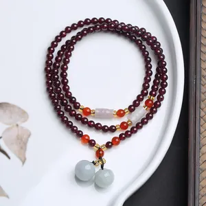 Makroaufnahme von Granat Armband mit Jade-Anhängern auf weißer Keramikschale