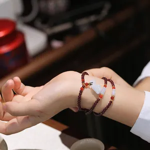 Detail eines mehrlagigen Granatarmbands mit Jade-Anhänger am Handgelenk einer Frau