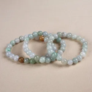 Detail of three natural jade beaded bracelets in soft green and white hues on beige texture