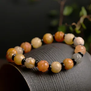 Natural gold silk jade bracelet with carved lotus beads on a dark ceramic vessel