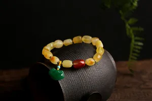 Close-up of a natural beeswax bead bracelet featuring a green ruyi lock on a ceramic jar