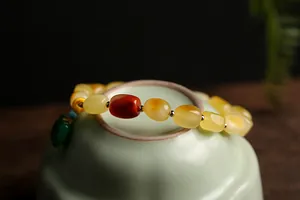 Detail of amber beeswax style bracelet with jadeite lock charm on green teacup