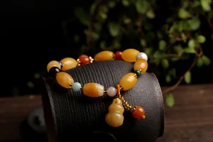 Close-up of yellow jade beaded bracelet with colorful accents and gourd pendant on pottery