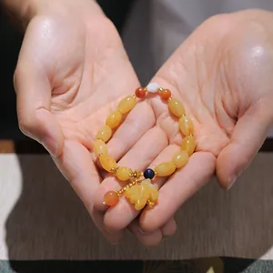 Detailed view of yellow gemstone beaded bracelet with leaf charm held in hands