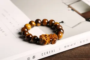 Detalle macro de cuentas naturales de ojo de tigre y dije Pixiu tallado en la pulsera