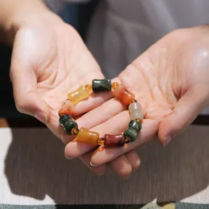 Macro shot of multi-color jade beads bracelet with pumpkin and drum shapes in human hands