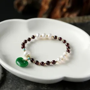 Garnet and freshwater pearl beaded bracelet with a green jade leaf pendant on white plate