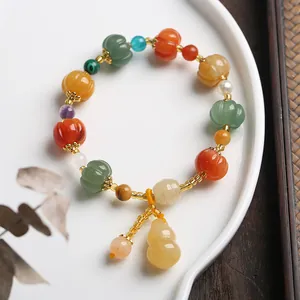 Detailed shot of multi-color pumpkin bead bracelet with jade gourd charm on ceramic tray