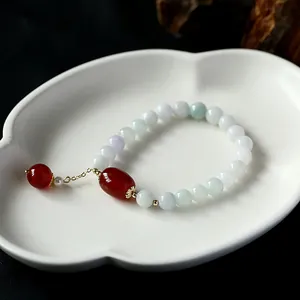Detail of beaded jade bracelet with red agate barrel bead and gold-plated tassel on ceramic tray