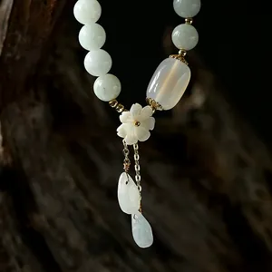 Detail view of 14K gold-filled jade bracelet featuring shell flower and water-drop pendants