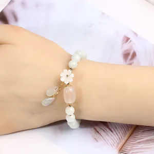Close-up of jade bead bracelet with shell flower and water-drop pendants on a wrist