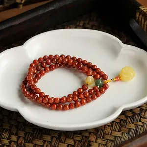 Detail of red agate bracelet with a carved amber rose pendant on a white ceramic tray