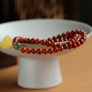 Detail of red agate beads bracelet with a yellow leaf charm on a white ceramic bowl