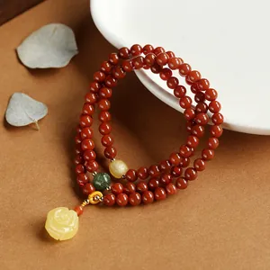 Macro view of multi-strand red agate bracelet with carved amber rose charm and gold spacers