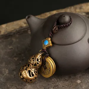 Vintage hollow brass gourd keychain with fish patterns and ancient coins on dark stone