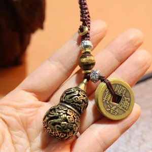 Macro detail of brass gourd pendant with tiger eye stone and antique coins on woven cord