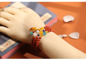 Detail van een meerlaagse rode kralenarmband met turquoise en barnsteen bedeltjes