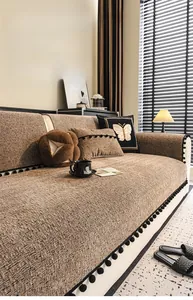 Detail of brown chenille sofa cover with thick texture and black pom-pom fringe trim