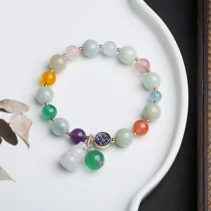 Detail of colorful gemstone beads bracelet with a purple gourd pendant on a white ceramic plate