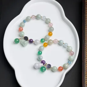 Detailed view of colorful beaded jade bracelets with gourd charm in white ceramic dish