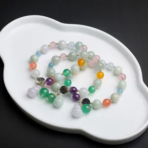 Detailed close-up of jade gourd charms and natural gemstone beads on a white ceramic tray