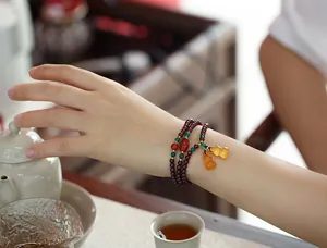 Three-wrap garnet beaded bracelet with jadeite gourds on wrist with tea set background