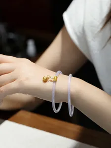 Detalle del brazalete fino de calcedonia lila suave con un dije de campana dorada