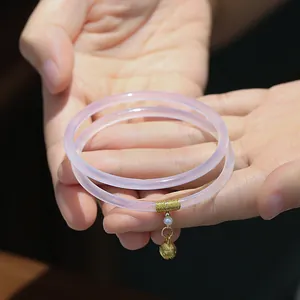 Primer plano de dos pulseras finas de calcedonia rosa con colgante dorado y perla