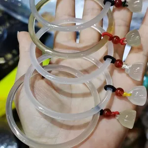 Detalle de cinco pulseras de ágata translúcida con dijes de loto verde en la mano