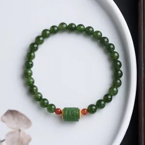 Macro shot of green jasper bead bracelet with carved cylinder bead on white plate
