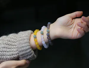 Dettaglio di tre braccialetti di perle in agata naturale gialla e lilla sul polso