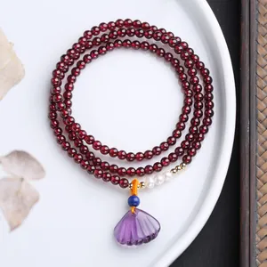 Detail of triple-layer garnet bracelet with amethyst shell pendant on white ceramic plate