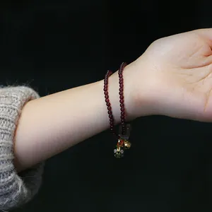 Detalle de pulsera de granate con cascabel dorado y dije de esmalte en la muñeca mujer