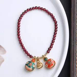Detalle de pulsera de granate con cascabeles de esmalte de colores y amuleto dorado en plato