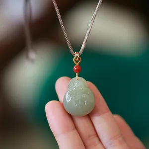 Vue macro du pendentif Bouddha en jade néphrite sculpté avec perle rouge et cordon tressé
