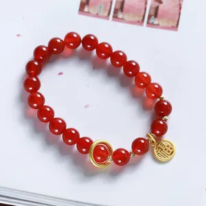 Detail of 8mm red agate bead bracelet featuring a gold Fu character charm on a book