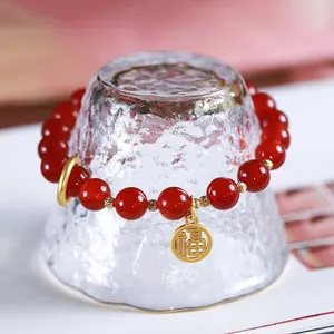 8mm red agate beaded bracelet with gold Fu pendant displayed on a frosted glass