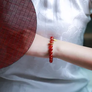 Macro detail of 8mm red agate bead bracelet with golden Fu charm on a female wrist