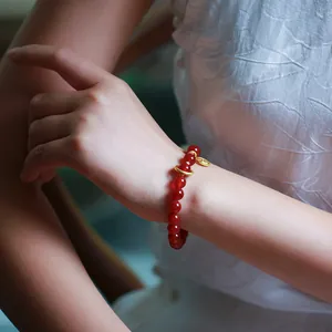Close-up of 8mm red agate bead bracelet with golden fortune pendant on wrist