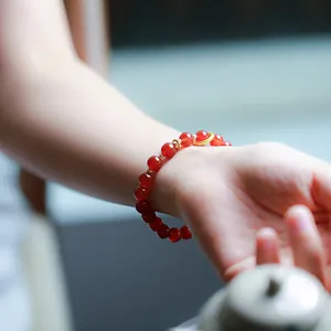 Macro shot of 8mm red agate beaded bracelet with gold charms on a woman's wrist