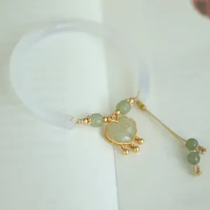 Close-up of Ruyi lock pendant on white chalcedony jade bracelet with gold accents
