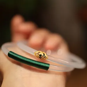 Close-up of translucent white jadeite bangle with green silk wrap and gold ruyi detail
