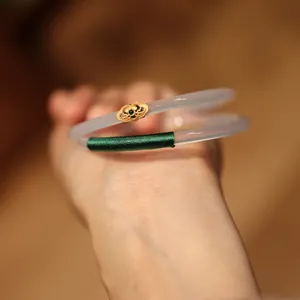 Close-up of chalcedony bangles with gold floral accents and dark green thread wrapping