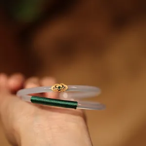 Detail of white chalcedony bangle with gold Ruyi ornament and green thread wrap