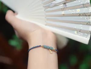 Nahaufnahme eines handgewebten blauen Kordelarmbands mit Jadestücken und Goldanhänger